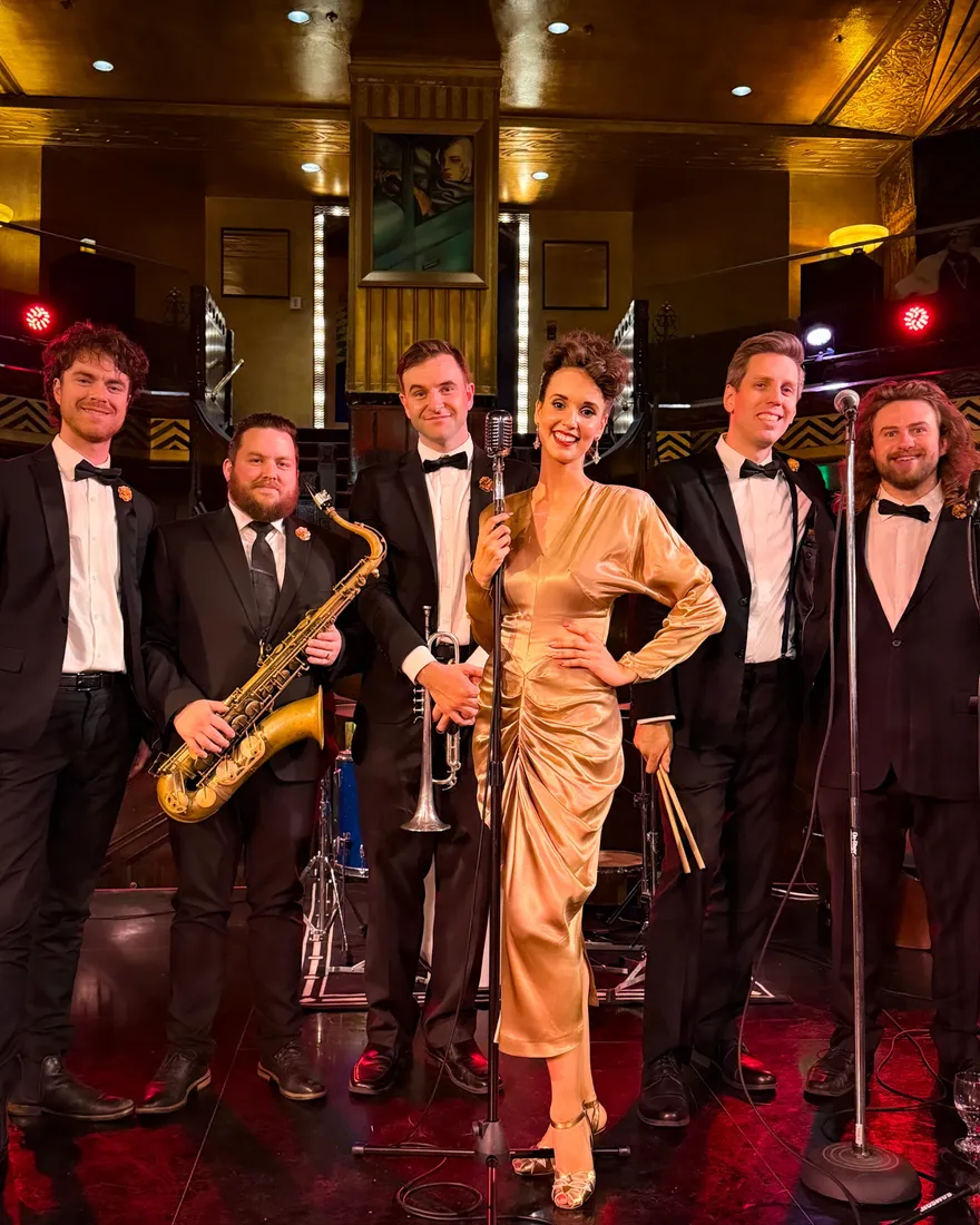 Ashley Anne in a gold satin gown with The Carnations in black tie on the Art Deco stage of the Cicada Club in Los Angeles