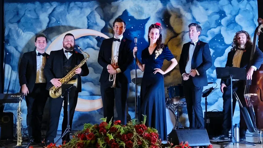 Ashley Anne in a navy velvet gown with the full six-piece Carnations ensemble in black tie, in front of a painted moon-and-clouds backdrop