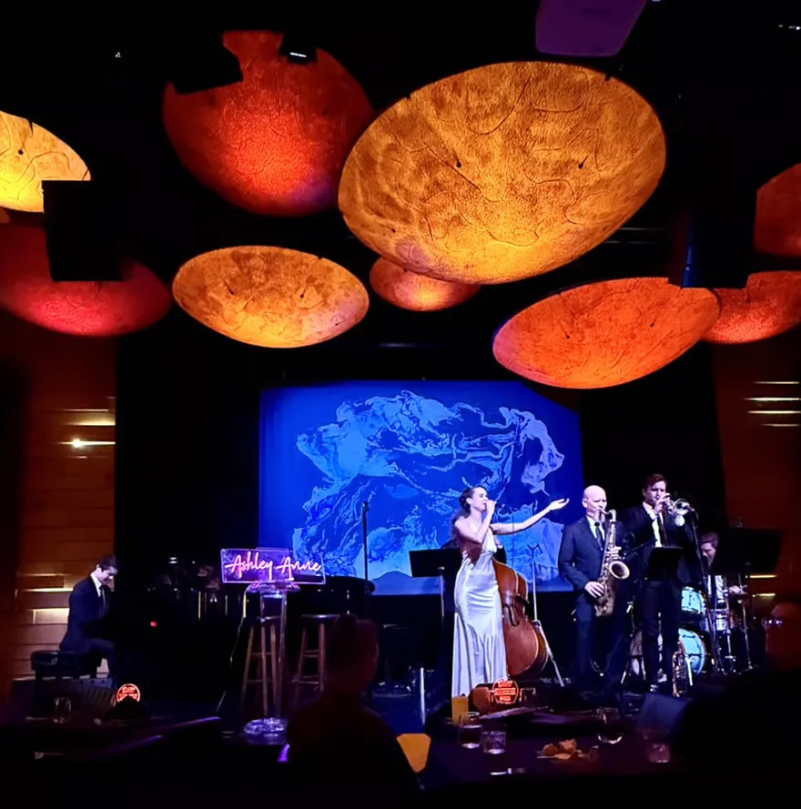 Ashley Anne performing a featured set with horn players under warm lights at an upscale venue