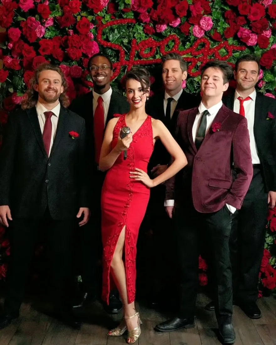 Ashley Anne in a red gown with The Carnations in front of the rose wall at Spago Beverly Hills