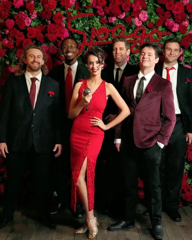 Ashley Anne in a red gown with The Carnations in front of the rose wall at Spago Beverly Hills