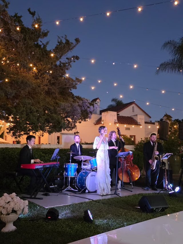 Band playing under string lights at dusk beside the dance floor of a Spanish-style estate wedding